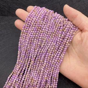 Detailed view of 2mm faceted natural purple phosphorite beads held by hand for scale