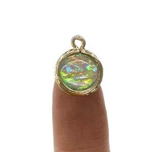 Iridescent round crystal pendant with gold textured edge held on fingertip for size