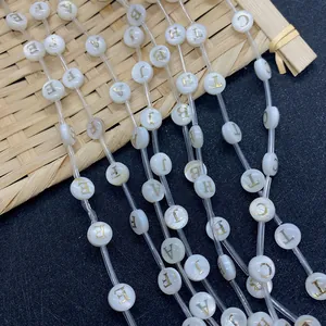 Macro view of 8mm white shell beads with golden engraved letters on a bamboo tray