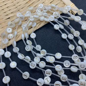 Detail of 8mm white shell beads with golden engraved letters on natural bamboo tray