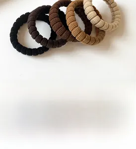 Detail of five elastic ribbed hair ties in earth tones like coffee and beige on white background