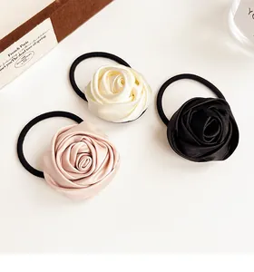 Close-up of three satin rose hair scrunchies in pink, beige, and black colors
