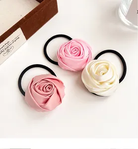 Three satin rose hair ties in pink and cream arranged on a clean white backdrop