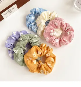 Flat lay of six colorful floral scrunchies with white daisy patterns on soft fabric