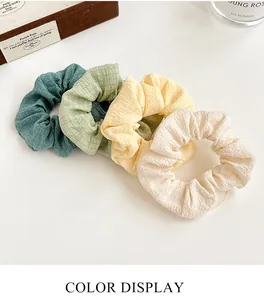 Close-up of four pleated fabric scrunchies in green, yellow, and cream on a white surface
