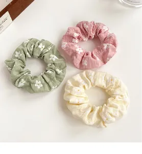 Three colorful floral scrunchies in pastel tones with daisy patterns on a white background
