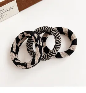 Detail of three knitted checkerboard hair ties in black and beige with zebra patterns