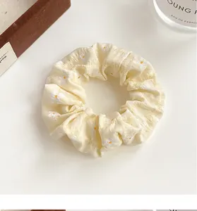 Close-up of yellow floral fabric scrunchie with soft pleats and elastic texture