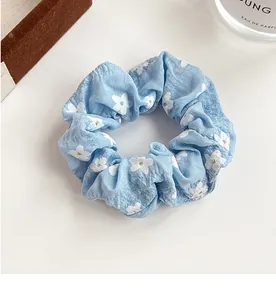 Detail of light blue floral scrunchie with white flower print on a white surface