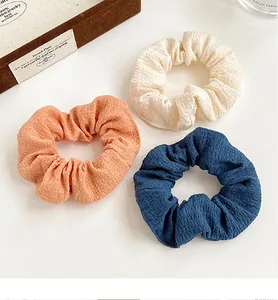 Close-up of three textured bubble fabric scrunchies in cream, coral pink and navy blue