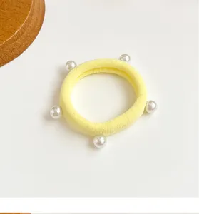 Gros plan d'un élastique à cheveux jaune clair avec cinq perles blanches brillantes