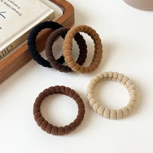 Five pieces of coffee-toned elastic ribbed hair ties on a rustic wooden tray and books