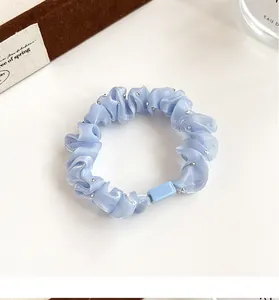 Détail d'un chouchou plissé bleu clair avec strass brillants et texture soyeuse fine