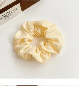 Detail view of a cream-colored scrunchie showing bubble texture and soft elastic fabric