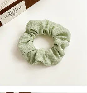 Close-up of light green textured fabric hair scrunchie with soft plaid pattern detail