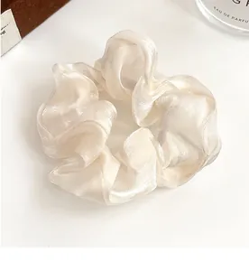 Gros plan d'un chouchou en soie crème nacrée avec une texture douce et des plis élégants