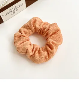 Detail of orange scrunchie with bubble texture fabric and elastic band on white surface