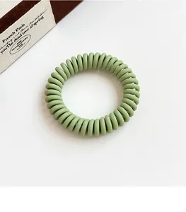 Macro detail of matte bean green spiral hair coil on a minimalist white aesthetic backdrop