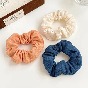 Set of 3 textured seersucker scrunchies in beige, orange, and blue for high ponytail