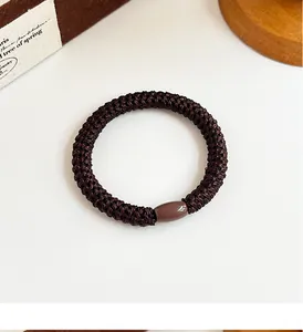 Detail of coffee brown braided hair tie with smooth resin bead on a minimalist background