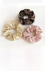 Détail de trois chouchous plissés nacrés en or rose et marron sur fond blanc