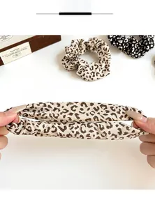 Detail showing the high elasticity and sewing of a leopard print scrunchie stretched by hand