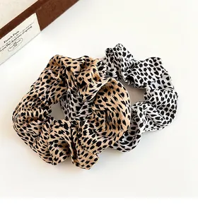 Detailed view of two leopard print scrunchies in khaki and white on a white background