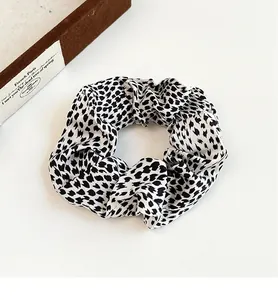 Close-up of black and white polka dot scrunchie with soft fabric pleats on white surface