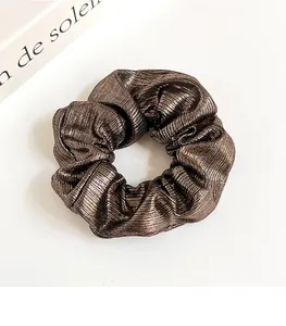 Détail d'un chouchou plissé bronze métallique avec éclat satiné sur fond blanc