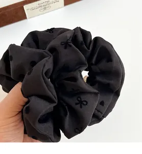 Close-up of black ribbed fabric scrunchie with flocking bow and polka dot patterns