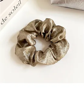 Détail d'un chouchou doré métallique avec texture plissée sur fond blanc élégant