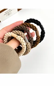 Detail of high-elastic braided hair ties in coffee tones held by hand for durability test
