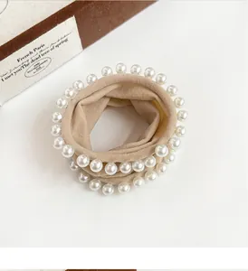 Detail of beige fabric scrunchie with high-gloss pearls and soft pleated texture