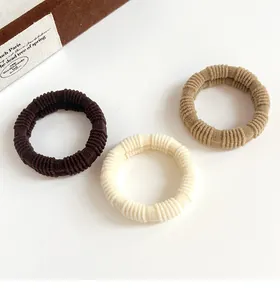 Macro detail of three elastic ribbed hair ties in coffee, cream, and beige earth tones