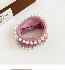 Close-up of pink elastic hair tie with elegant white pearls on a soft fabric texture