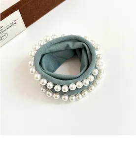 Close-up of greyish-green wide scrunchie with white faux pearls on white surface
