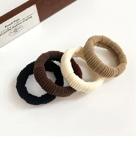 Detail of four ribbed elastic hair ties in neutral colors including black and cream