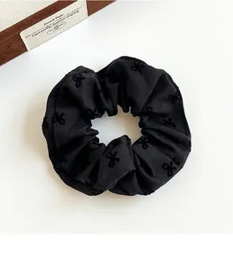 Detail of black fabric scrunchie with textured bow embroidery on white background