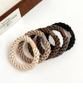 Detail of five braided elastic hair ties in gradient earth tones on a clean white background