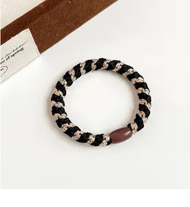 Détail d'un élastique tressé noir et doré avec une perle marron brillante de luxe