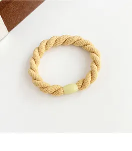 Gros plan d'un élastique à cheveux tressé épais beige avec boucle ovale verte