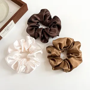 Tre elastici scrunchie in raso premium color crema, caffè e marrone su fondo chiaro