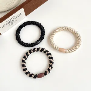 Lot de trois chouchous tressés élastiques noir et or sur un fond blanc épuré