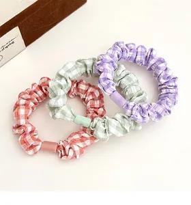 Close-up detail of three plaid fabric scrunchies with decorative acrylic buckles