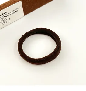 Gros plan d'un chouchou marron foncé à haute élasticité sur fond blanc minimaliste