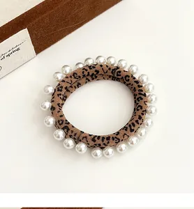 Detail of leopard print scrunchie with faux pearls on soft brown suede fabric texture