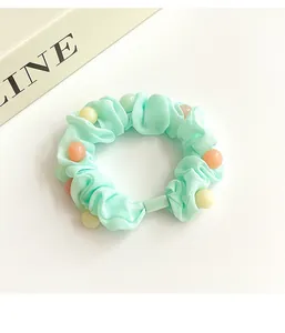 Détail d'un chouchou vert menthe avec perles macarons et texture de tissu doux
