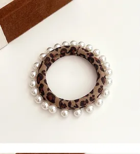 Detailed close-up of leopard print hair tie with small white pearls on beige background