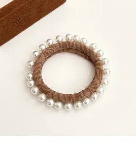 Detail of brown fabric hair tie with elegant white pearls on a minimalist background