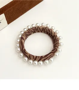 Detailed view of leopard print hair tie with elegant white pearls on fabric